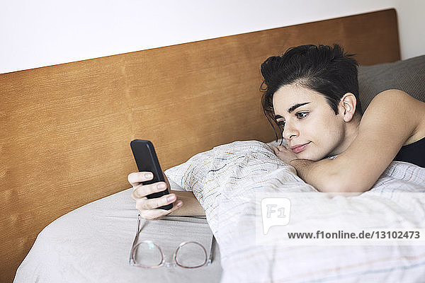Hochwinkelansicht einer Frau  die ein Mobiltelefon benutzt  während sie sich im Bett entspannt