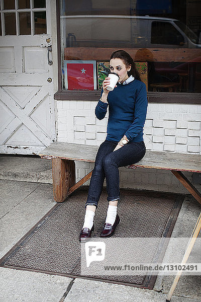 Frau sitzt auf Bank und trinkt Kaffee