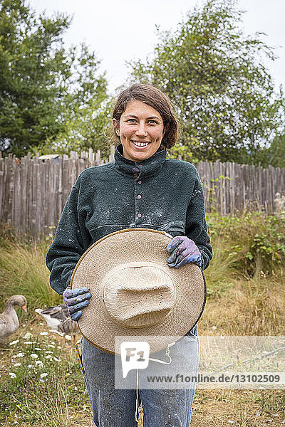 Porträt einer glücklichen Bienenzüchterin  die einen Hut hält  während sie auf einem Bauernhof steht