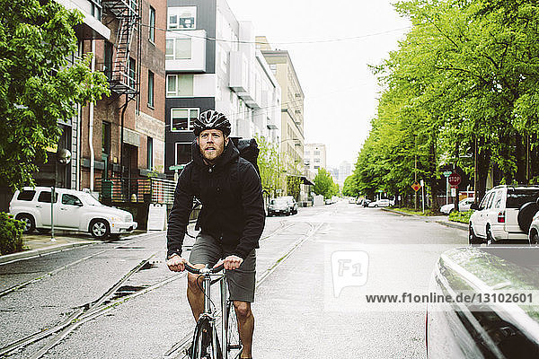 Männlicher Pendler fährt Fahrrad auf nasser Straße gegen den Himmel