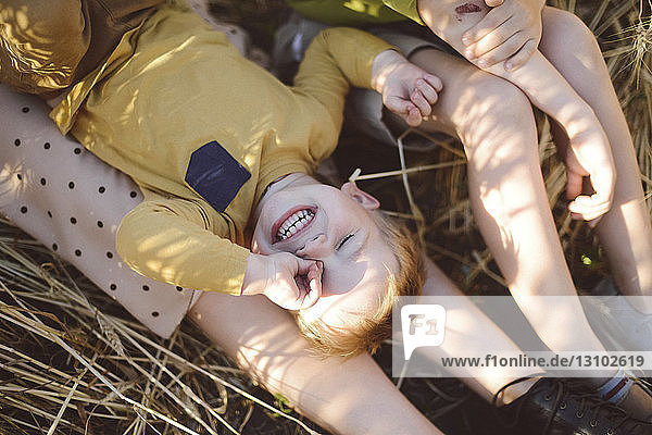 Boy rubbing eye while lying on mother's legs by brother on field