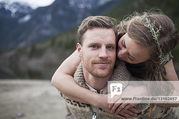 Portrait of boyfriend while girlfriend embracing him against mountains
