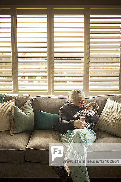 Grandmother playing with baby grandson on sofa at home