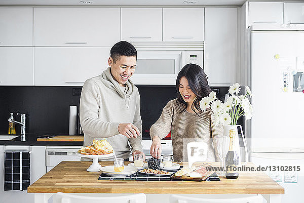 Glückliches Paar beim Frühstück  während es in der Küche am Esstisch steht