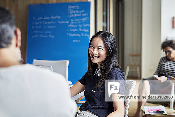 Lächelnde Geschäftsfrau plant mit Kollegin im Vorstandszimmer im Kreativbüro
