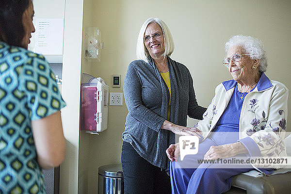 Lächelnde Patientin mit Tochter schaut den Arzt an  während sie auf der Krankenhausstation sitzt