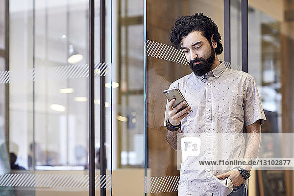 Businessman using smart phone while standing at doorway in office