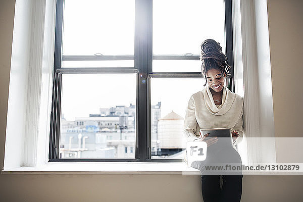 Smiling businesswoman using digital tablet while sitting at window