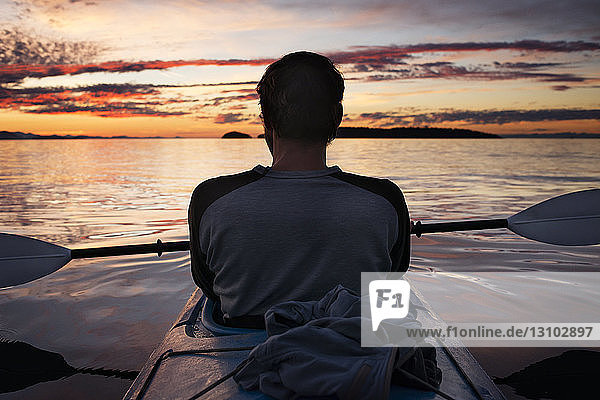 Rückansicht eines Mannes  der sich bei Sonnenuntergang im Kajak entspannt