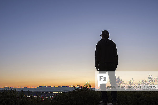 Silhouette man looking at view while standing on mountain against clear sky during sunset