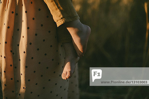 Midsection of mother with son on field during sunset