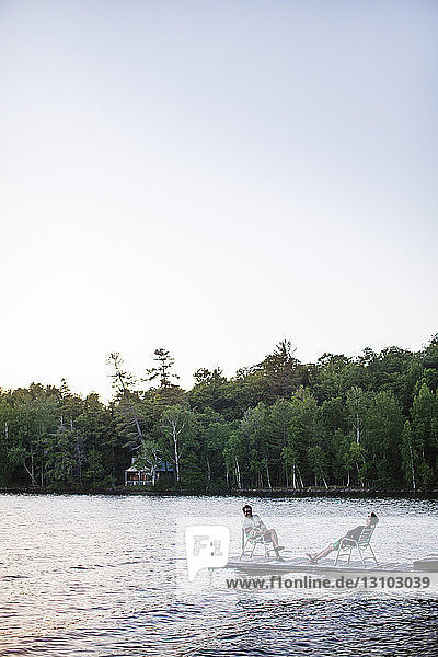 Freunde entspannen sich auf einem Steg am See bei klarem Himmel