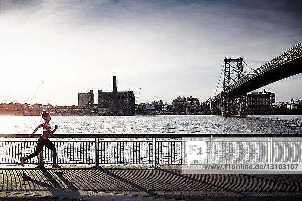 Entschlossene Frau joggt auf der Promenade mit der Williamsburg-Brücke im Hintergrund