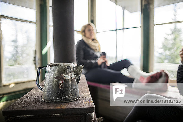 Kettle on table by woman relaxing on window in cottage