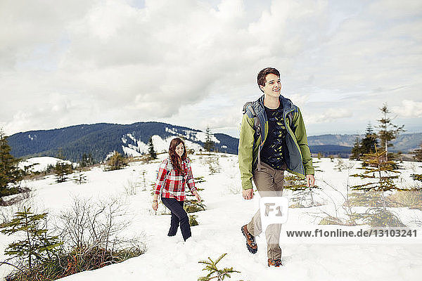 Happy friends hiking on snow covered field against cloudscape