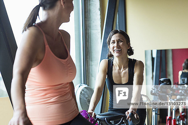 Freundinnen unterhalten sich  während sie im Fitnessstudio auf Heimtrainern sitzen