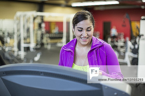 Lächelnde Frau hört Musik  während sie im Fitnessstudio auf dem Laufband trainiert