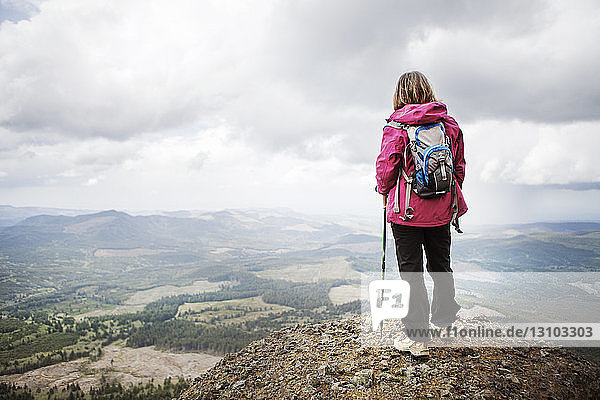 Rear view of female hiker with backpack standing on mountain against cloudy sky