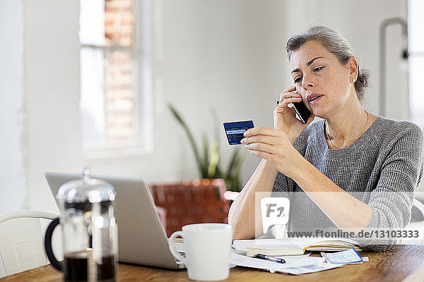 Frau hält Debitkarte  während sie zu Hause telefoniert