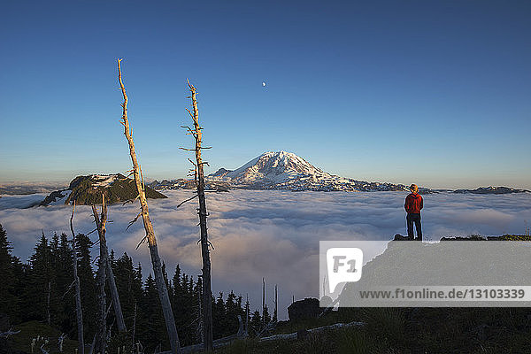 Rückansicht eines männlichen Wanderers  der bei Sonnenaufgang auf einem Berg durch eine Wolkenlandschaft steht