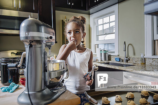 Cute girl eating while preparing chocolate chip cookies in kitchen