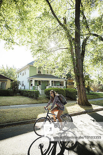 Full length of woman cycling on road against houses