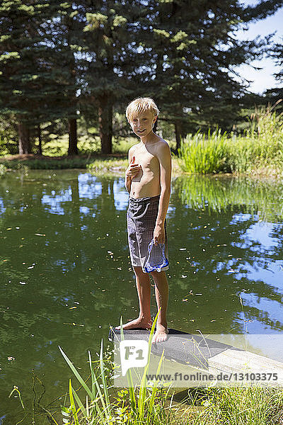 Porträt eines Jungen  der auf einem Sprungbrett am Seeufer steht