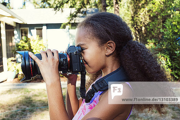 Side view of girl photographing through digital camera while standing in yard