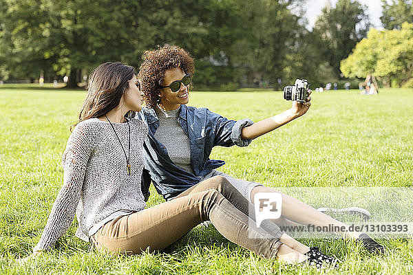 Freunde fotografieren  während sie im Park auf dem Feld sitzen
