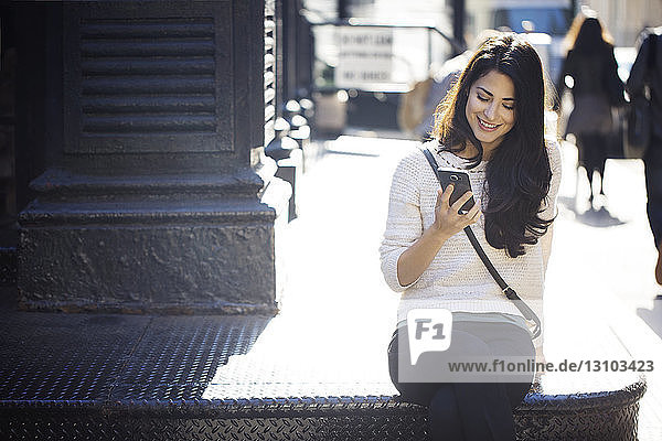 Glückliche junge Frau benutzt Smartphone auf Treppen im Freien