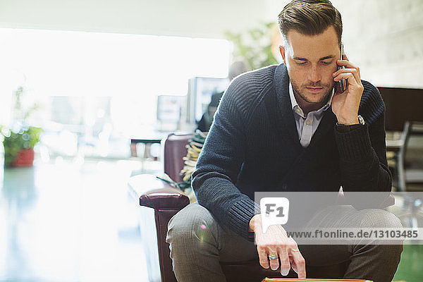 Businessman talking on mobile phone while sitting on chair in office