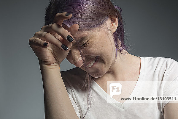 Junge Frau mit gefärbten Haaren schaut weg und zuckt vor grauem Hintergrund