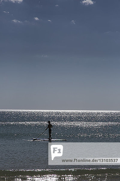 Silhouette paddle boarder on sunny summer ocean