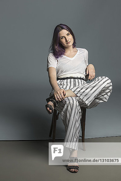 Portrait confident and fashionable young woman sitting on chair against gray background