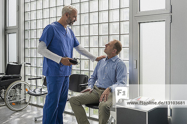 Männlicher Arzt spricht mit einem Patienten im Wartezimmer einer Klinik und tröstet ihn