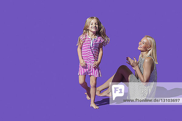 Portrait playful mother and daughter in striped dresses against purple background