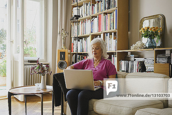 Senior woman using laptop on living room sofa