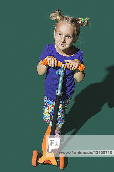 Porträt selbstbewusstes Mädchen fährt Roller gegen grünen Hintergrund
