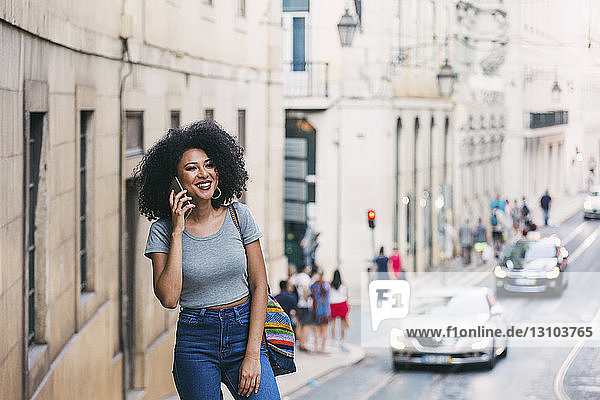 Lächelnde junge Frau  die auf einer städtischen Straße mit einem Smartphone spricht  Lissabon  Portugal
