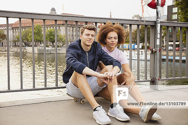 Portrait junges Paar auf Skateboard sitzend auf städtischer Brücke