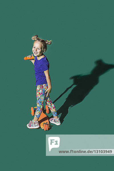 Unbekümmertes Mädchen fährt Roller vor grünem Hintergrund