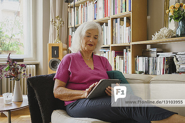 Ältere Frau mit digitalem Tablet auf dem Wohnzimmersofa
