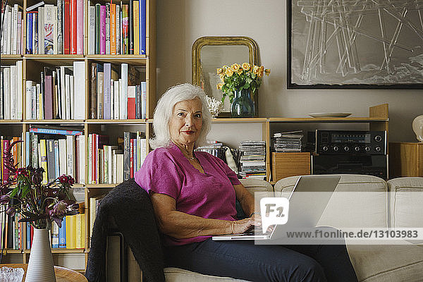 Portrait confident senior woman using laptop on living room sofa