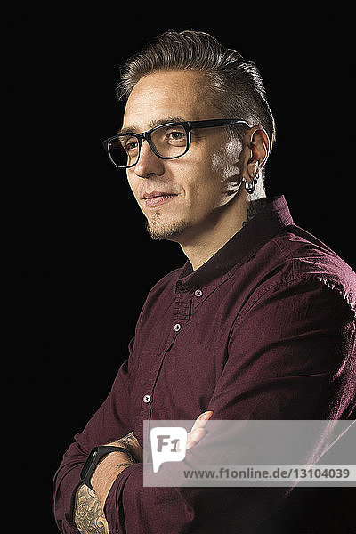 Portrait of man with glasses and arms crossed against black background