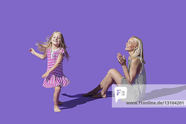 Mother watching daughter dancing on purple background