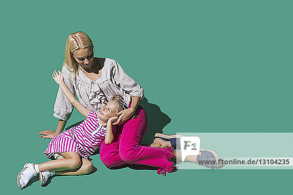 Mother and daughter talking against green background