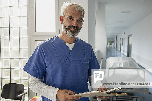Portrait confident male doctor with medical chart in hospital corridor