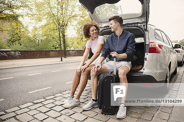Young couple with suitcase sitting in car hatchback