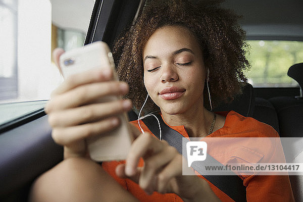 Gelassene junge Frau  die auf dem Rücksitz eines Autos mit Kopfhörern und mp3-Player Musik hört