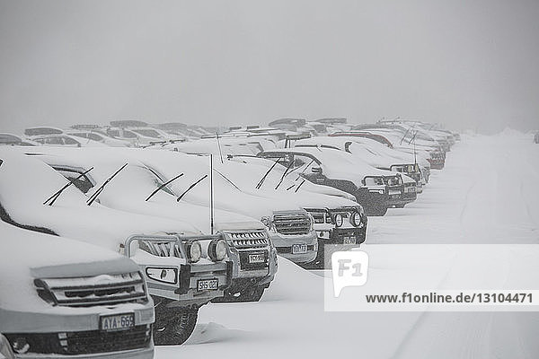 Schnee bedeckt geparkte Autos auf einem vollen Parkplatz